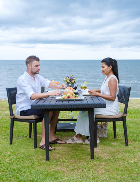Akşamları sahilde romantik bir akşam yemeği yiyen iki erkek ve kadın. Asyalı kadınlar ve beyaz erkekler Huahin Tayland sahilinde yemek yiyorlar. - Fotoğraf, Görsel