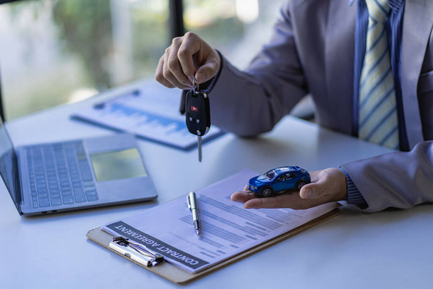 Концепция продаж автомобилей, торговые представители дают ключи клиентам на столе с небольшими образцами автомобилей и офисной страховкой. - Фото, изображение