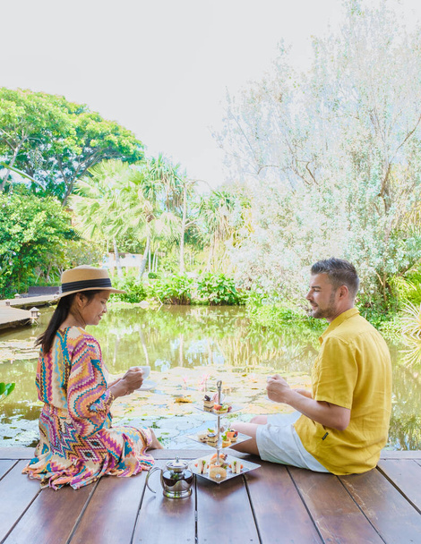 Délutáni tea egy tónál, tea egy thaiföldi trópusi kertben. Férfiak és nők egy trópusi kertben teáznak. - Fotó, kép