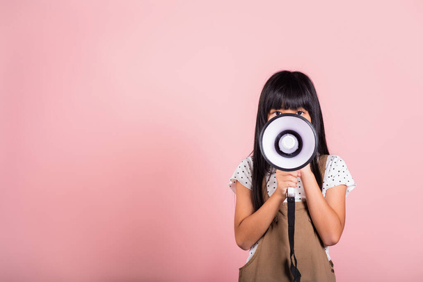 Asian little kid 10 years old shouting by megaphone at studio shot isolated on pink background, Happy child girl lifestyle she screeching through in megaphone announces discounts - Fotoğraf, Görsel