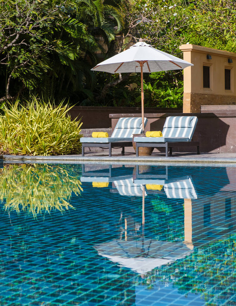 Lüks bir tatil köyünde palmiye ağaçları ve plaj sandalyeleri olan tropik bir havuz, okyanusa bakan palmiye ağaçları olan bir havuz. Havuzda plaj havlusu olan plaj sandalyeleri - Fotoğraf, Görsel