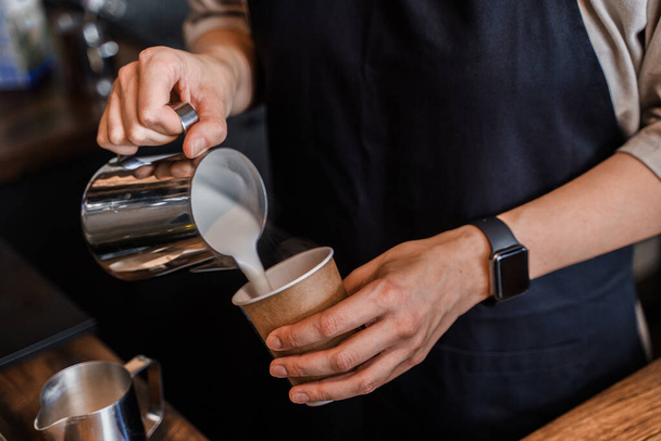 Tiros de mulher barman com avental preparando leite para café no café. - Foto, Imagem