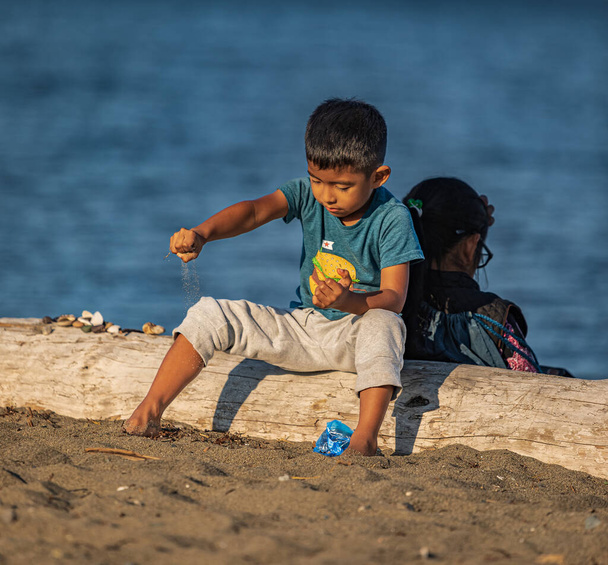Gelukkige jongen die met zand speelt in de buurt van de oceaan. Een peuter die op het strand speelt. Zomervakantie. Reisfoto, selectieve focus-15 september 2022-Vancouver BC Canada - Foto, afbeelding