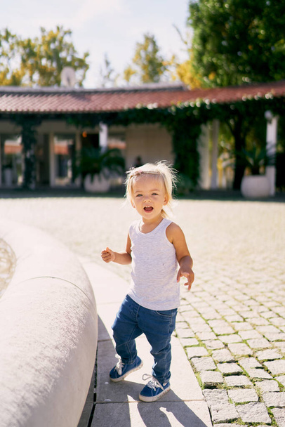 Ein kleines Mädchen steht lachend auf einer Fliese neben einem runden Zaun. Hochwertiges Foto - Foto, Bild