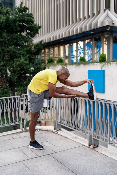 African American man stretching his left leg over railing in the city, - Photo, Image