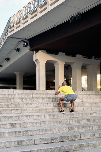 Rear view of an unrecognizable African American man doing squats exercises on stairs outdoor - Zdjęcie, obraz
