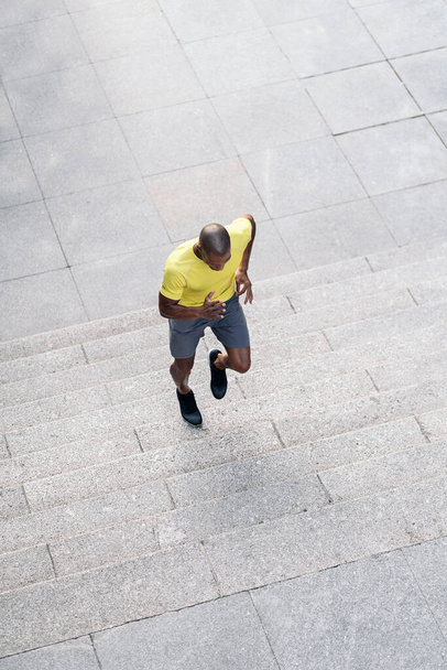 Aerial view of an African American sportsman with yellow t-shirt and shorts jogging up on stairs outdoors. - Foto, Imagem