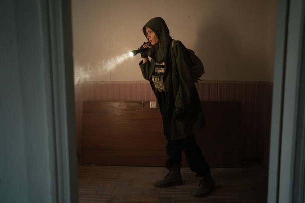 Женщина исследователь с фонариком внутри коридора или туннеля разрушенной фабрики промышленных зданий, ужас и жуткая атмосфера, постапокалиптический выживший винтажный тонированный - Фото, изображение