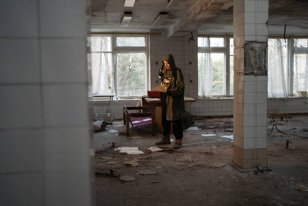 Nuclear post apocalypse life after doomsday concept. Grimy female survivor reading in abandoned building indoor - Photo, Image