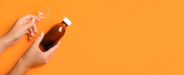 Mani femminili in possesso di bottiglia di sciroppo per la tosse e cucchiaio su sfondo arancione con spazio per il testo - Foto, immagini