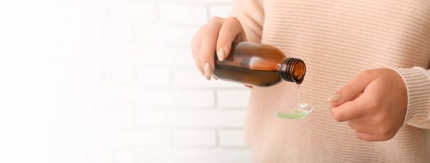 Vrouw giet hoestsiroop van fles in lepel, close-up. Banner voor ontwerp - Foto, afbeelding