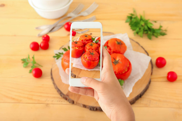 Γυναίκα φωτογράφος τροφίμων με κινητό τηλέφωνο λήψη φωτογραφιών νόστιμα γεμιστά τομάτες σε ξύλινο τραπέζι - Φωτογραφία, εικόνα
