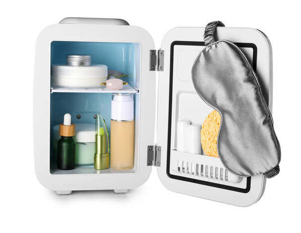 Small refrigerator with cosmetic products and sleeping mask on white background - Photo, Image