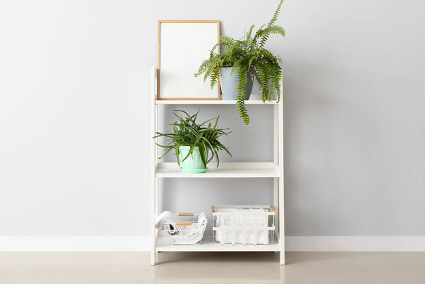 Shelving unit with houseplants, blank frame and towels near light wall - Photo, Image