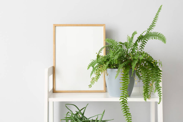 Shelving unit with houseplant and blank frame near light wall - Photo, Image