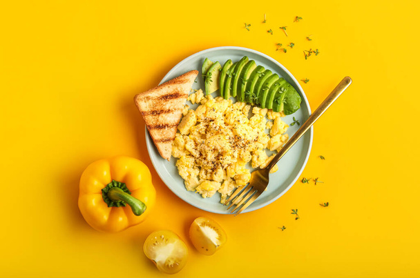 Composición con plato de sabrosos huevos revueltos, tostadas y aguacate sobre fondo amarillo - Foto, imagen