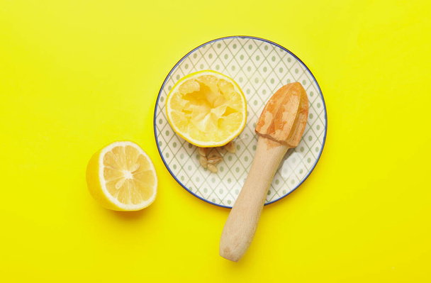 黄色の背景に新鮮なレモンと木製のジューサーとプレート - 写真・画像