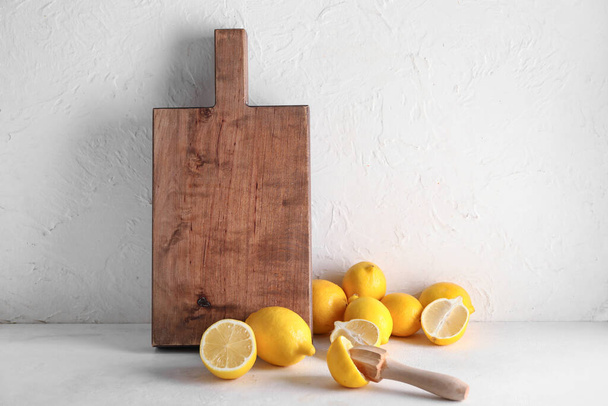 Holzbrett, frische reife Zitronen und Saftpresse auf hellem Tisch - Foto, Bild