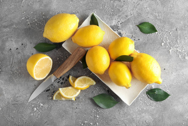 Plate with ripe lemons and knife on grunge background - Foto, Imagen