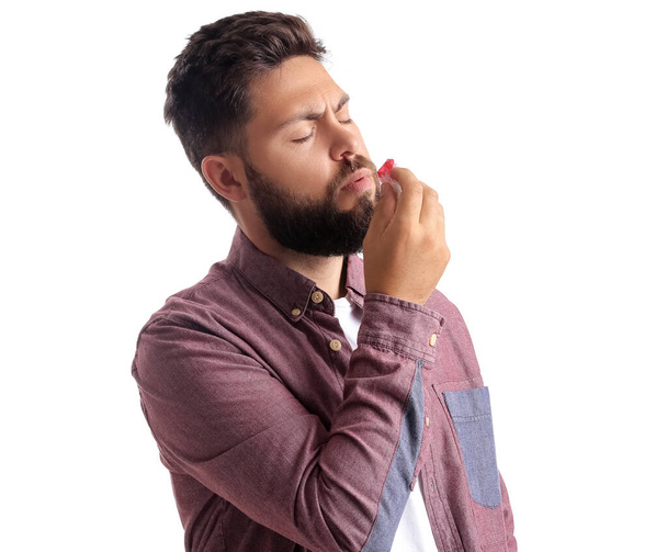 Homem barbudo jovem com sangramento nasal e tecido no fundo branco - Foto, Imagem