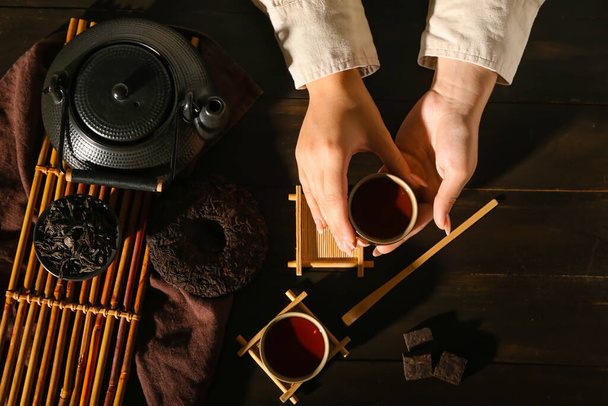 Kobiece ręce z filiżanką gorącej czystej herbaty i suchymi liśćmi tłoczonymi na ciemnym drewnianym stole - Zdjęcie, obraz