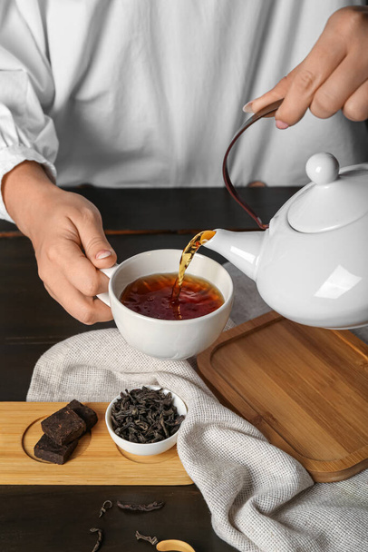 Γυναίκα ρίχνει ζεστό puer τσάι σε σκούρο ξύλινο τραπέζι, closeup - Φωτογραφία, εικόνα