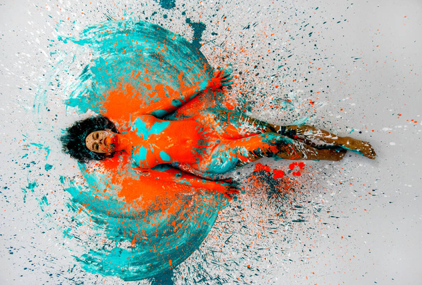 felülnézet szexi meztelen nő fekszik elegáns a padlón türkiz kék narancs színű absztrakt festett testfestés lány fröccsent földre, másolás tér - Fotó, kép