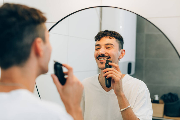 young adult man trimming hos mustaches in bathroom - 写真・画像