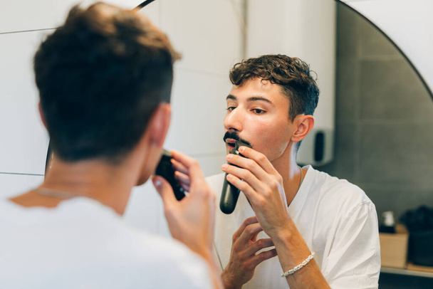 young adult man trimming hos mustaches in bathroom - Photo, Image