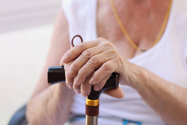 Ηλικιωμένος συνταξιούχος που κρατιέται χέρι-χέρι σε ξυλόγλυπτο κοντινό πλάνο. Κουρασμένος ώριμος συνταξιούχος που αναπαύεται μετά από επίπονο περπάτημα με ασκό - Φωτογραφία, εικόνα