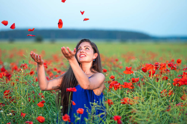elegant young woman with long hair playing with petals in poppy field in evening sunlight - Fotoğraf, Görsel