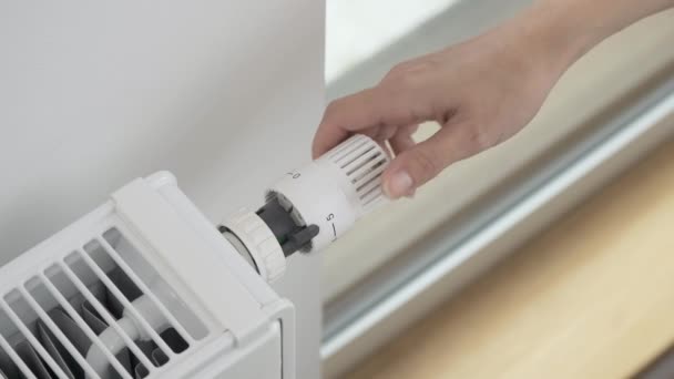 La mujer gira el regulador de la válvula termostática del radiador para aumentar la temperatura del calentador en la habitación al máximo. Calefacción del apartamento en clima frío y heladas severas - Metraje, vídeo