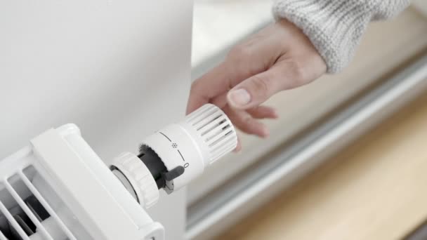 Nainen kääntyy jäähdyttimen termostaattisen venttiilin säädin lisäämään huoneen lämmittimen lämpötilaa maksimiin. Lämmitys huoneisto kylmällä säällä ja vaikea pakkaset - Materiaali, video