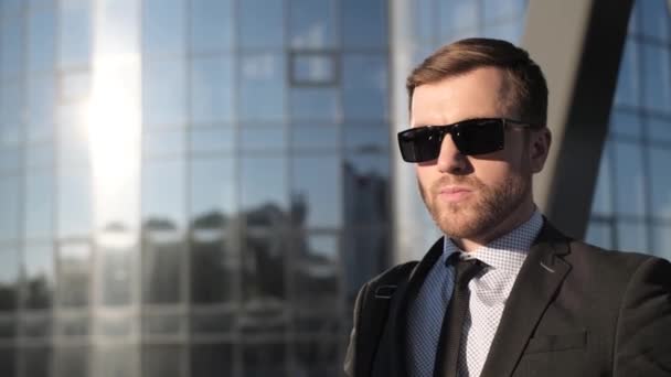 Portrait of a young businessman in sunglasses, he is standing against a background of a cloud. American business man - Footage, Video
