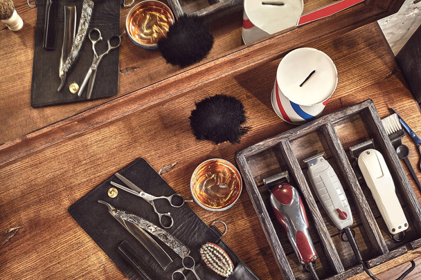 Hairdresser tools on wooden background. Top view on wooden table with scissors, comb, hairbrushes and hairclips, trimmer. Barbershop, manhood concept - Фото, зображення