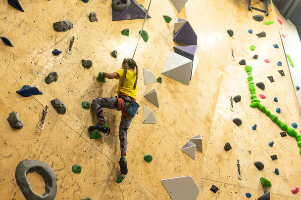 bouldering, niña trepando por la pared y escalador agarres multicolores. Actividades de ocio. - Foto, Imagen