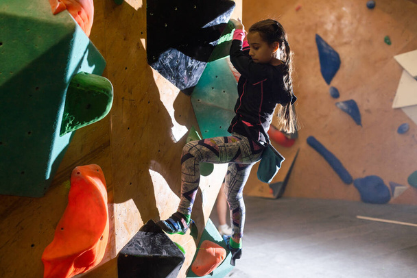 Junior Climber Girl shirt hanging on holds on climbing wall of indoor gym. - Foto, afbeelding