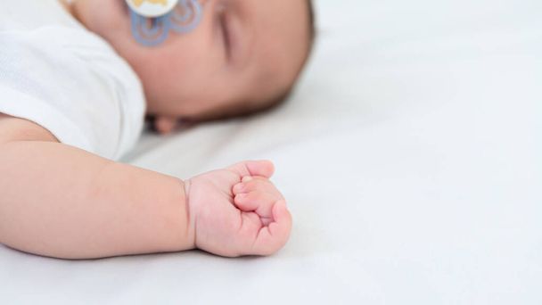 Крупним планом руки новонародженого хлопчика на білому фоні. Дитина спить на ліжку. Гарний концептуальний образ дитинства. Концепція сім'ї та дому з копіювальним простором
. - Фото, зображення