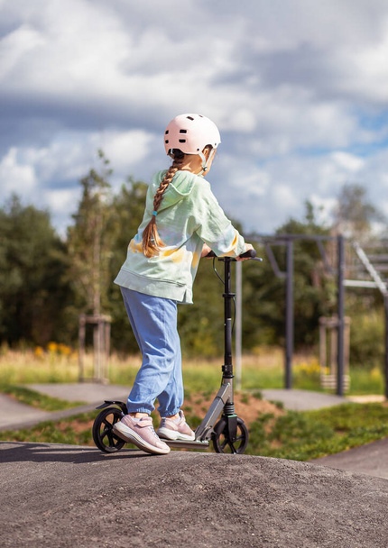  muotokuva söpö pieni valkoihoinen koulun tyttö käyttää kypärää nauttia hauskaa ratsastus skootteri asfaltoitu trackin katupuisto ulkona aurinkoisena päivänä. Terveellinen urheilu lasten toimintaa outsid - Valokuva, kuva
