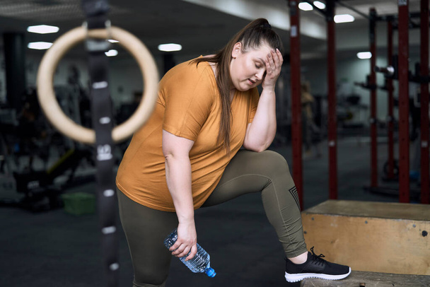 Mujer cansada con sobrepeso de pie en el gimnasio   - Foto, Imagen