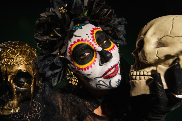 kobieta w czarny wieniec i kartina makijaż gospodarstwa czaszki izolowane na czarny  - Zdjęcie, obraz
