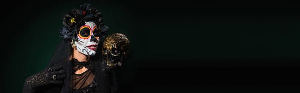 暗い緑の背景に頭蓋骨を保持するサンタミューティの衣装の女性,バナー  - 写真・画像