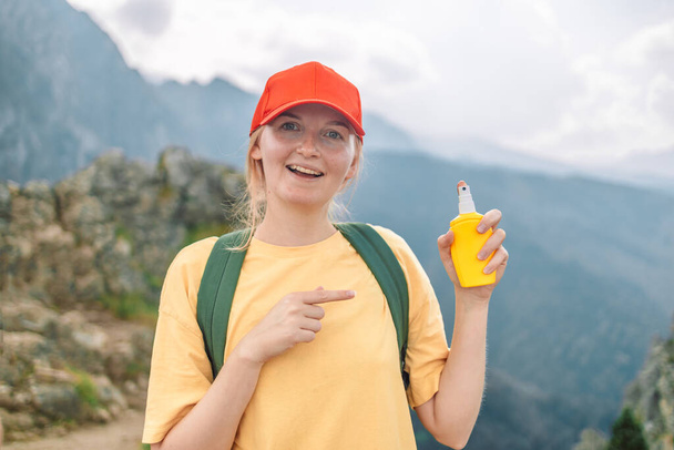 若い女性は、自然山の頂上でハイキング中にスプレーボトルで肌に虫よけを噴霧旅行します。虫刺されに対する皮膚保護.  - 写真・画像