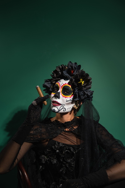 Woman in mexican day of death creepy costume holding cigar on green background  - Фото, зображення