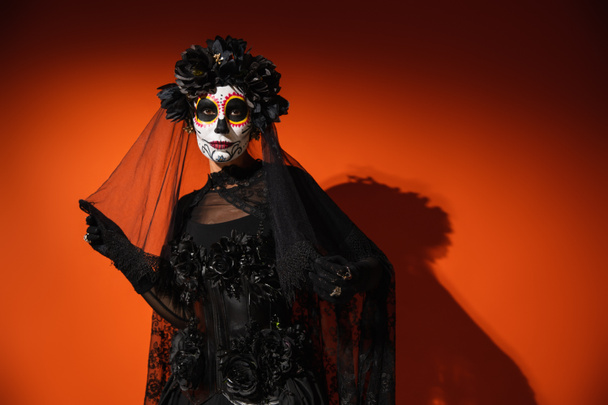 Mujer en halloween catrina maquillaje tocando velo negro sobre fondo rojo  - Foto, imagen