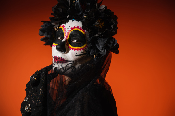 Portrait of woman with sugar skull makeup touching black veil on red background  - Photo, Image