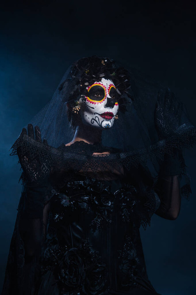 kobieta w strój czarownicy i makijaż czaszki cukru gospodarstwa koronki welon na ciemnoniebieskim tle - Zdjęcie, obraz