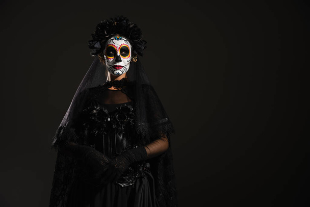 femme en costume sombre et effrayant et maquillage du crâne de sucre debout isolé sur noir - Photo, image
