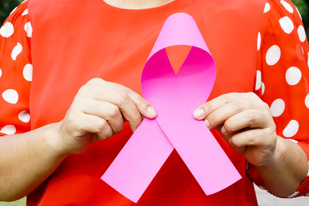 Kobieta z bliska trzyma różową papierową wstążkę. Koncepcja: Świadomość raka piersi. Rozchmurzcie chorych na raka na całym świecie.                                     - Zdjęcie, obraz