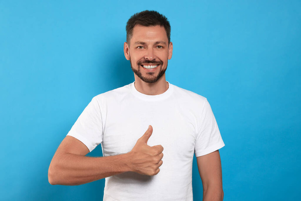 Man showing thumb up on light blue background - Foto, afbeelding